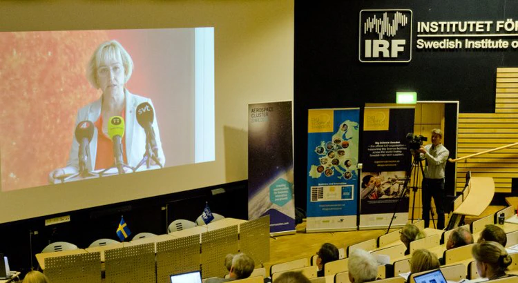 Pressträffen med Helene Hellmark Knutsson visas på storbildsskärm i IRF:s aula i Kiruna Pressträffen med Helene Hellmark Knutsson visas på storbildsskärm i IRF:s aula i Kiruna