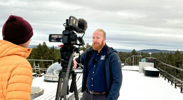 SVTs reporter intervjuar Daniel Kastinen på IRFs snötäckta tak, med mätutrustning under kupoler i bakgrunden SVTs reporter intervjuar Daniel Kastinen på IRFs snötäckta tak, med mätutrustning under kupoler i bakgrunden