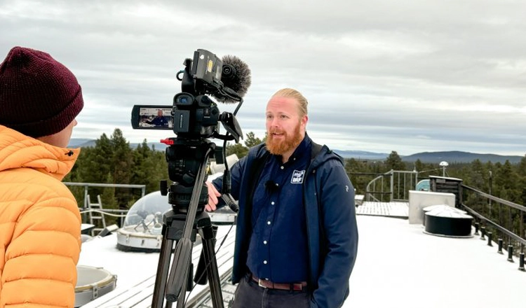 SVTs reporter intervjuar Daniel Kastinen på IRFs snötäckta tak, med mätutrustning under kupoler i bakgrunden