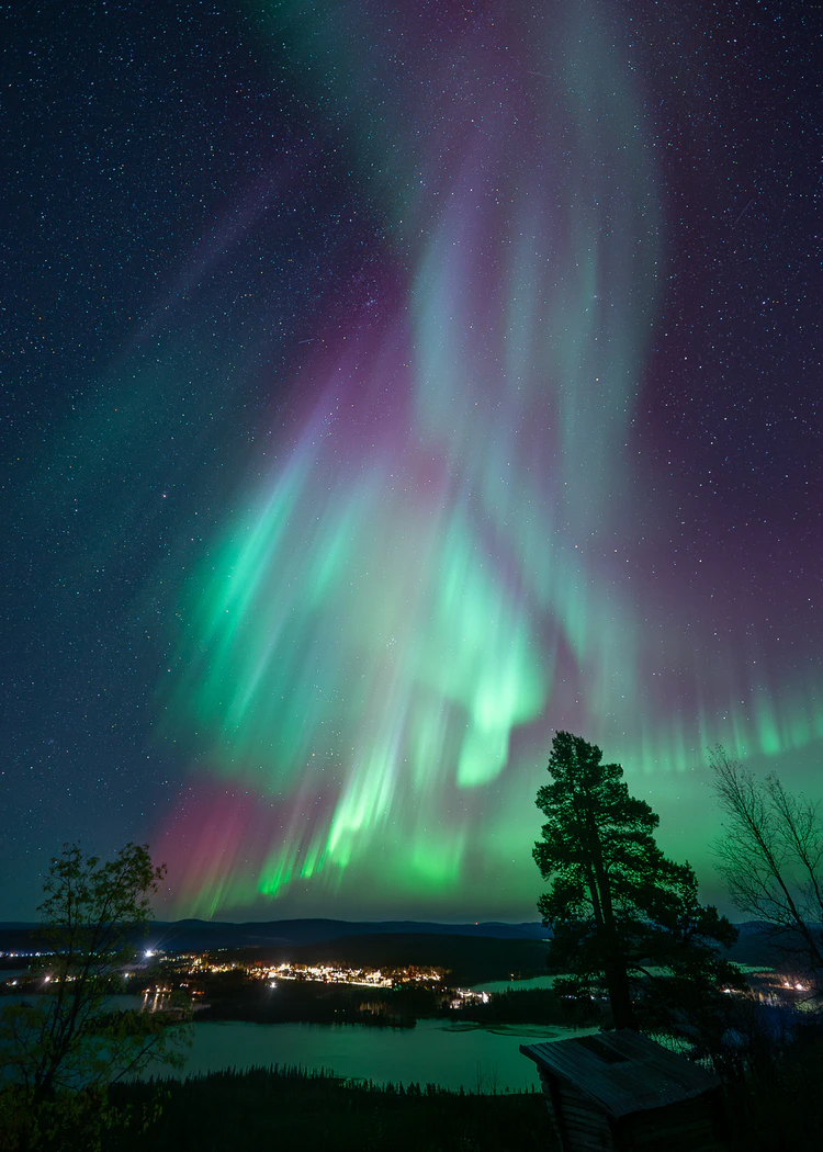 Lila norrsken över sjö och stad i fjärran
