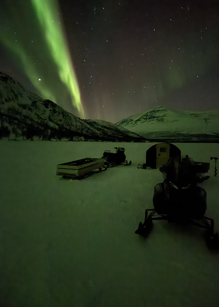 Skotrar ute på led med norrsken över himlen