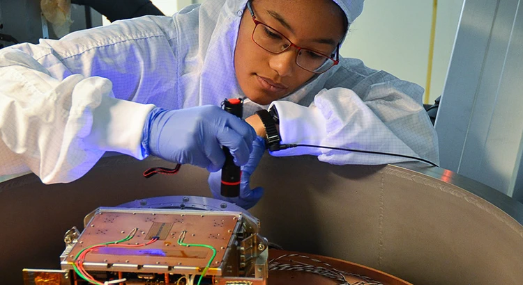 Engineer in protective clothing prepares instrument for test in vacuum chamber