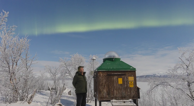 Person bredvid norrskensstation under norrskenshimmel